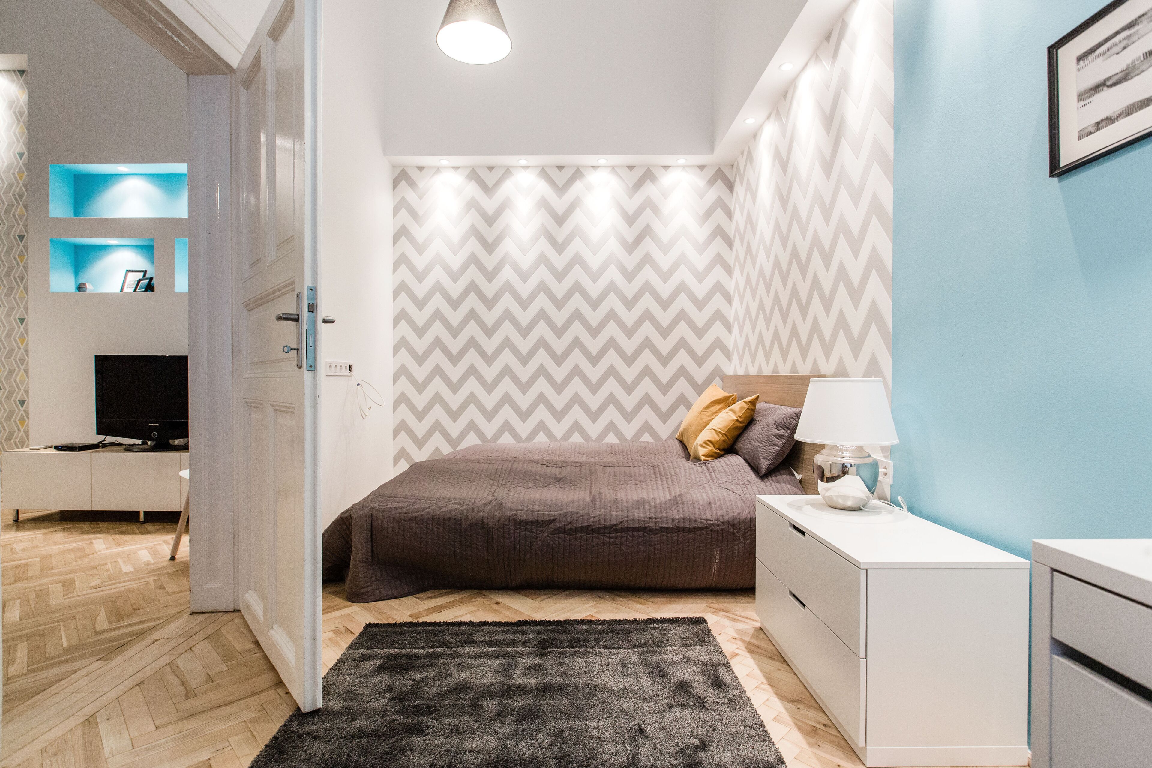 Une chambre à coucher avec un lit, une table de chevet, une lampe et un téléviseur posé sur un meuble.