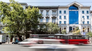 Un edificio de varios pisos con estilo arquitectónico clásico, que presenta una fachada central de vidrio azul y ventanas simétricas.