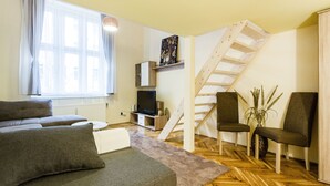 A living room with a sofa, chairs, a TV, a wooden staircase, and a window with curtains. - Balassi 27 Apartment (Budapest)