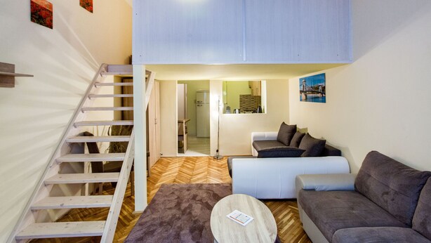 A compact living space with a loft bedroom, a staircase, a sofa, a coffee table, and a dining area. - Balassi 27 Apartment (Budapest)