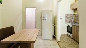 A compact kitchen with a refrigerator, stove, and wooden table. - Balassi 27 Apartment (Budapest)