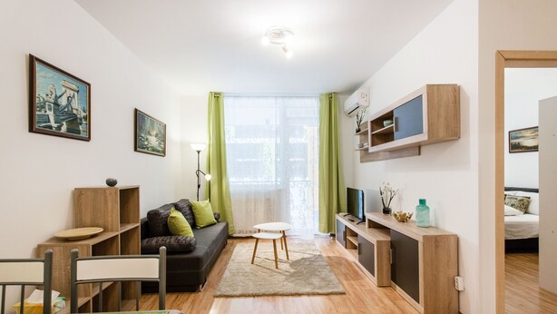 Una sala de estar moderna con un sofá, una mesa de comedor y sillas, una mesita redonda pequeña y un televisor sobre un soporte de madera.