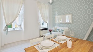 A dining area with a wooden table set for two, a white sofa, and a window with sheer curtains. - Dob 11 Apartment I. (Budapest)