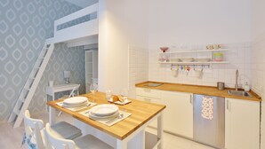 A modern kitchen with white cabinetry, a wooden countertop, and a built-in dishwasher. There is a dining area with a table set for two, and a ladder leading to a lofted space. - Dob 11 Apartment I. (Budapest)