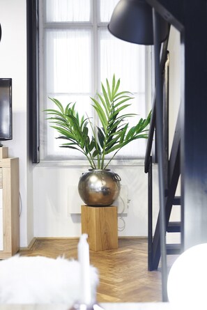 Een kamer met een potplant op een houten kruk, een zwarte vloerlamp en een televisie op een houten dressoir.