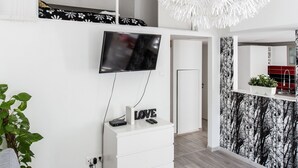 Uma sala de estar moderna com uma televisão de tela plana, um console branco, um lustre branco grande e uma parede estampada.
