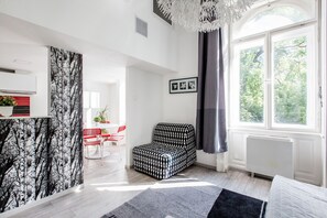 Ett modernt vardagsrum med en mönstrad soffa, en matplats med ett rött och vitt bord och ett stort fönster med utsikt över träd.
