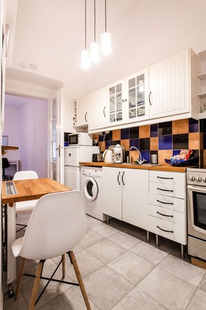 Una cocina compacta con armarios blancos, microondas, lavadora y estufa.