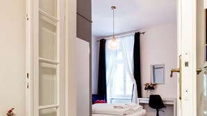 A bedroom with a bed, a desk, and a chair. There is a fire extinguisher on the wall.