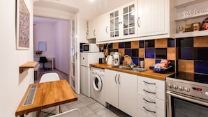 A compact kitchen with a washing machine, microwave, and oven. There is a wooden table and a chair.