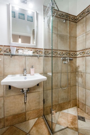 Un baño con ducha envuelta en vidrio, un lavamanos con espejo y azulejos decorativos en las paredes.