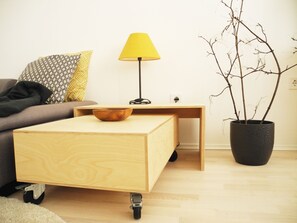 En hyggelig stue med sofa, lille træbord med lampe, skål og en potteplante.
