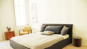 A modern bedroom with a large bed, a bedside table, a chair, and a small round table. - Harsfa 18 Apartment (Budapest)