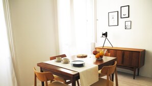 A dining area with a wooden table, chairs, and a bowl of fruit. There are framed pictures on the wall and a tripod in the background. - Harsfa 18 Apartment (Budapest)