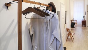 A hallway with a wooden coat rack holding a white shirt and a brown jacket. There is a dining area with a table and chairs in the background. - Harsfa 18 Apartment (Budapest)