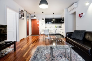 Una sala de estar moderna con una mesa de centro de vidrio, un sofá de cuero negro y un tapete estampado.