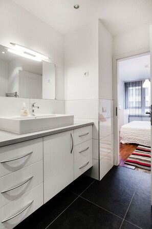 A modern bathroom with a white sink, mirror, and cabinet.
