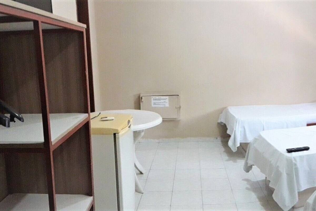 A hotel room with two single beds, a wooden wardrobe, a small bedside table, a window, and a bathroom with a toilet and sink.