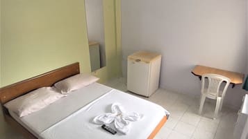 Una habitación de hotel con cama, un escritorio pequeño, una silla, un refrigerador y un espejo.