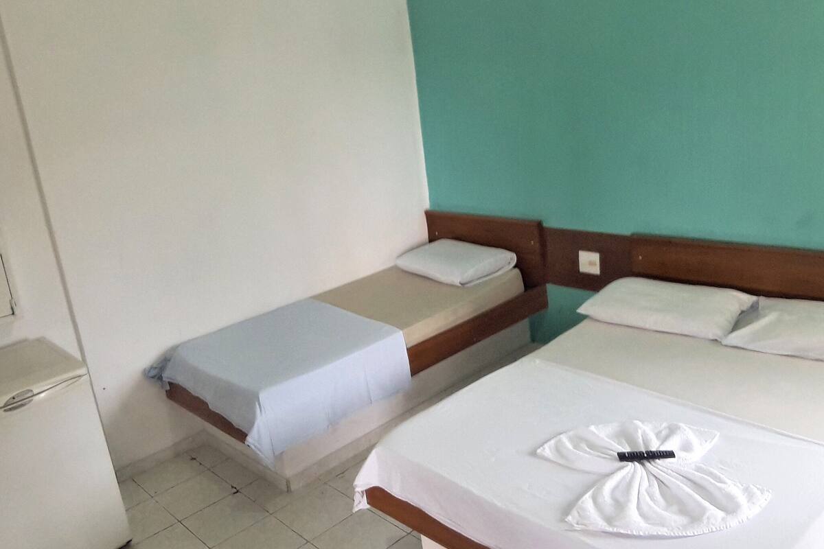 A hotel room with two beds, a small kitchenette, and a teal-colored wall.
