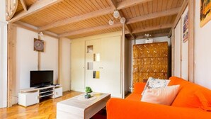 A modern living room with a wooden ceiling, a television on a white stand, a wooden coffee table, an orange sofa, and a patterned cabinet. - Hunyadi 3 Apartment (Budapest)
