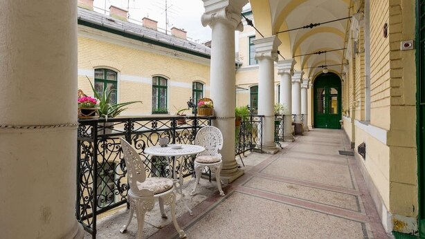 A covered outdoor corridor with white columns, a green door at the end, and a table with chairs. - Hunyadi 3 Apartment (Budapest)