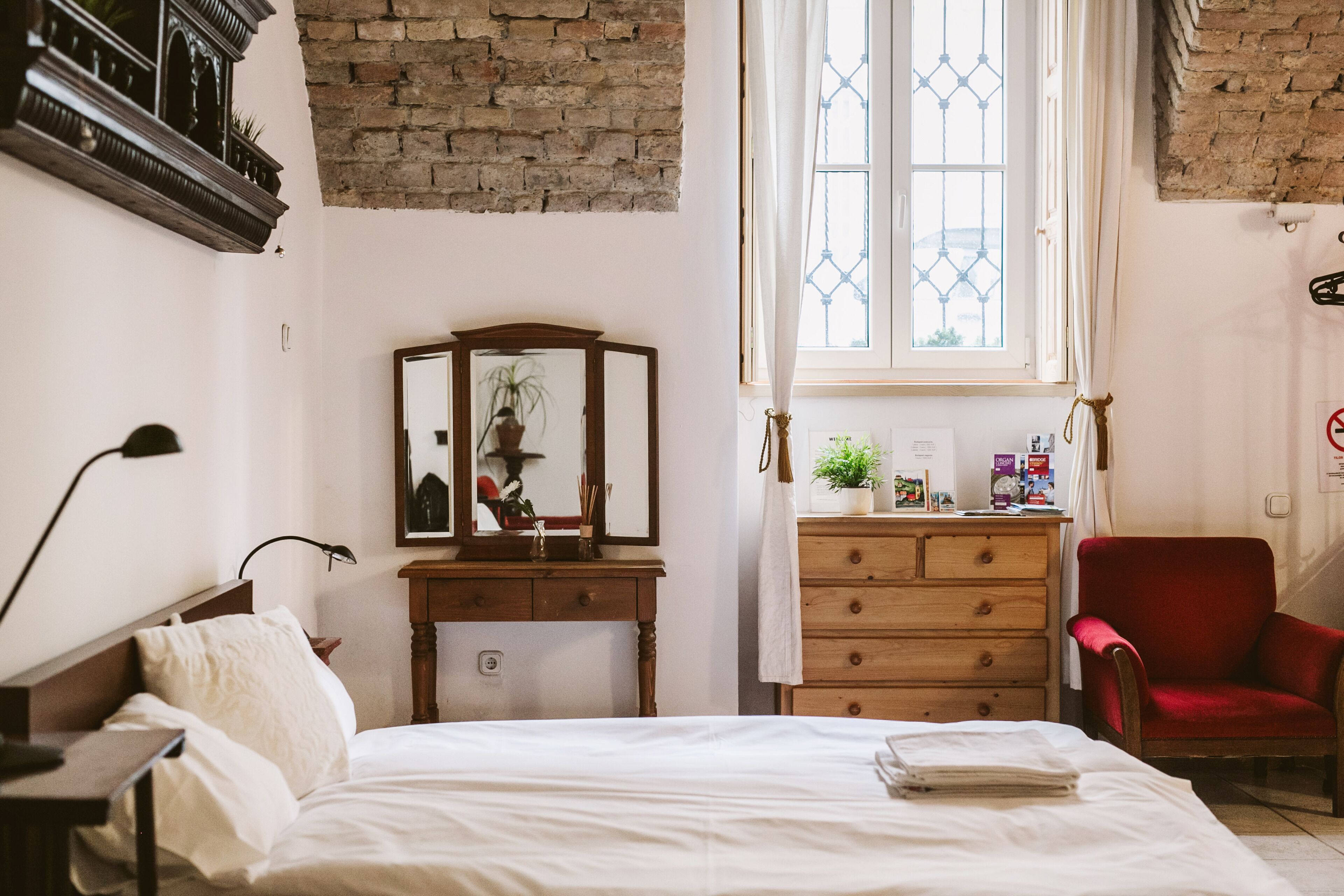 A bedroom with a bed, wooden dresser, red chair, and a window with curtains.