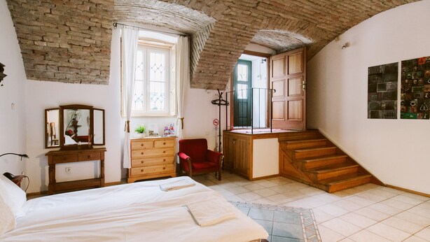Un dormitorio con una cama grande, un aparador de madera, una silla roja, una ventana con cortinas y una escalera que lleva a otra habitación.
