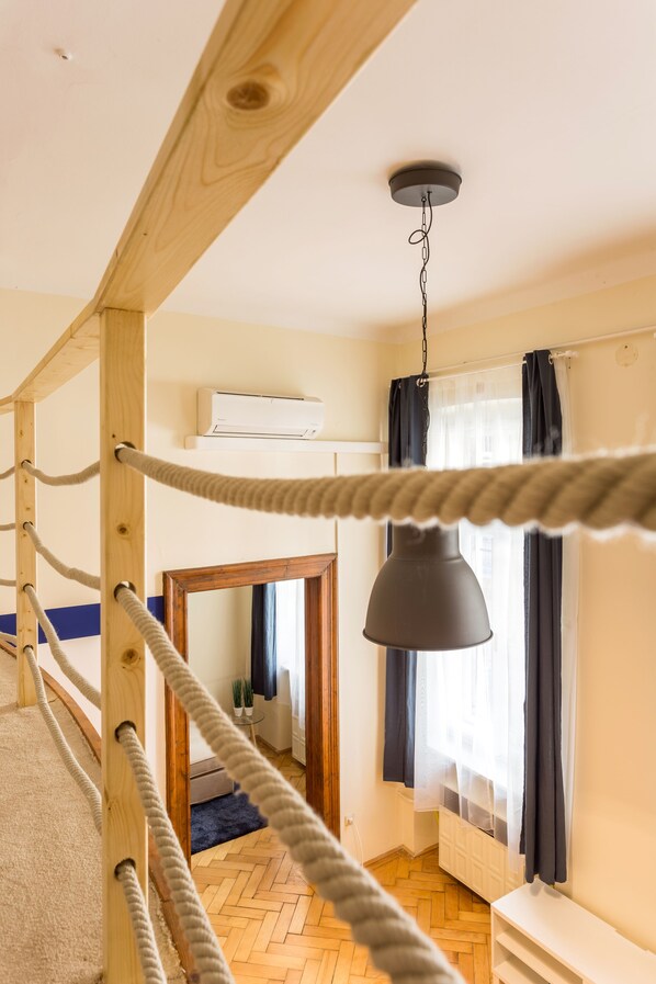 Una habitación con techo de madera, una lámpara colgante, una ventana con cortinas y un radiador.