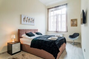 A modern bedroom with a bed, bedside table, lamp, artwork, window, and a chair. - Kazinczy 11 Apartment (Budapest)