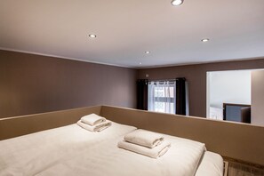 Hotelkamer met een groot bed, twee netjes gevouwen handdoeken, een raam met gordijnen en inbouwspots.
