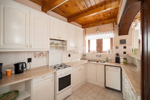 A kitchen with white cabinets, a stove, a dishwasher, and a window with curtains.