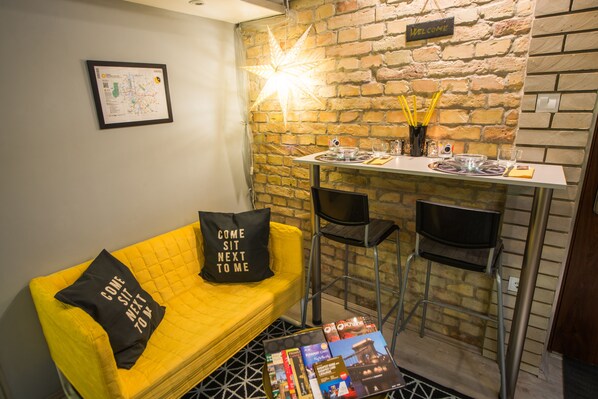 A cozy room with a yellow sofa, a small bar area, and a brick wall.