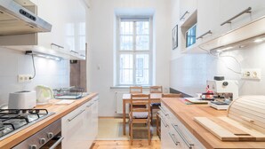 A modern kitchen with wooden countertops, a gas stove, a dining table with chairs, and a window providing natural light. - Kiraly 99 Apartment (Budapest)