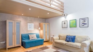 A modern living room with a blue sofa, beige sofa, and a wooden ceiling. There are three framed pictures on the wall and a small table with a lamp. - Kiraly 99 Apartment (Budapest)