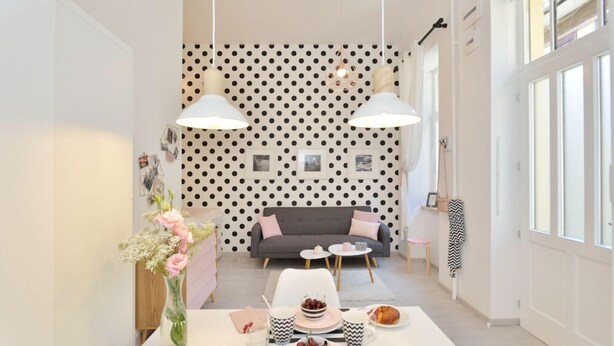 Un coin repas avec une table dressée pour deux personnes, un canapé gris et un papier peint à pois.