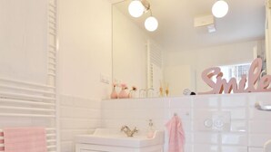 Une salle de bain avec des accessoires blancs, une serviette rose et un miroir avec éclairage intégré.