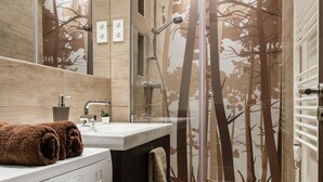 A modern bathroom with a glass shower enclosure, a built-in washing machine, and a large mirror. - Klauzal 10 Apartment (Budapest)