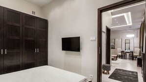 A bedroom with a bed, dark wooden wardrobe, a flat-screen TV, and a hallway leading to a bathroom. - Klauzal 10 Apartment (Budapest)