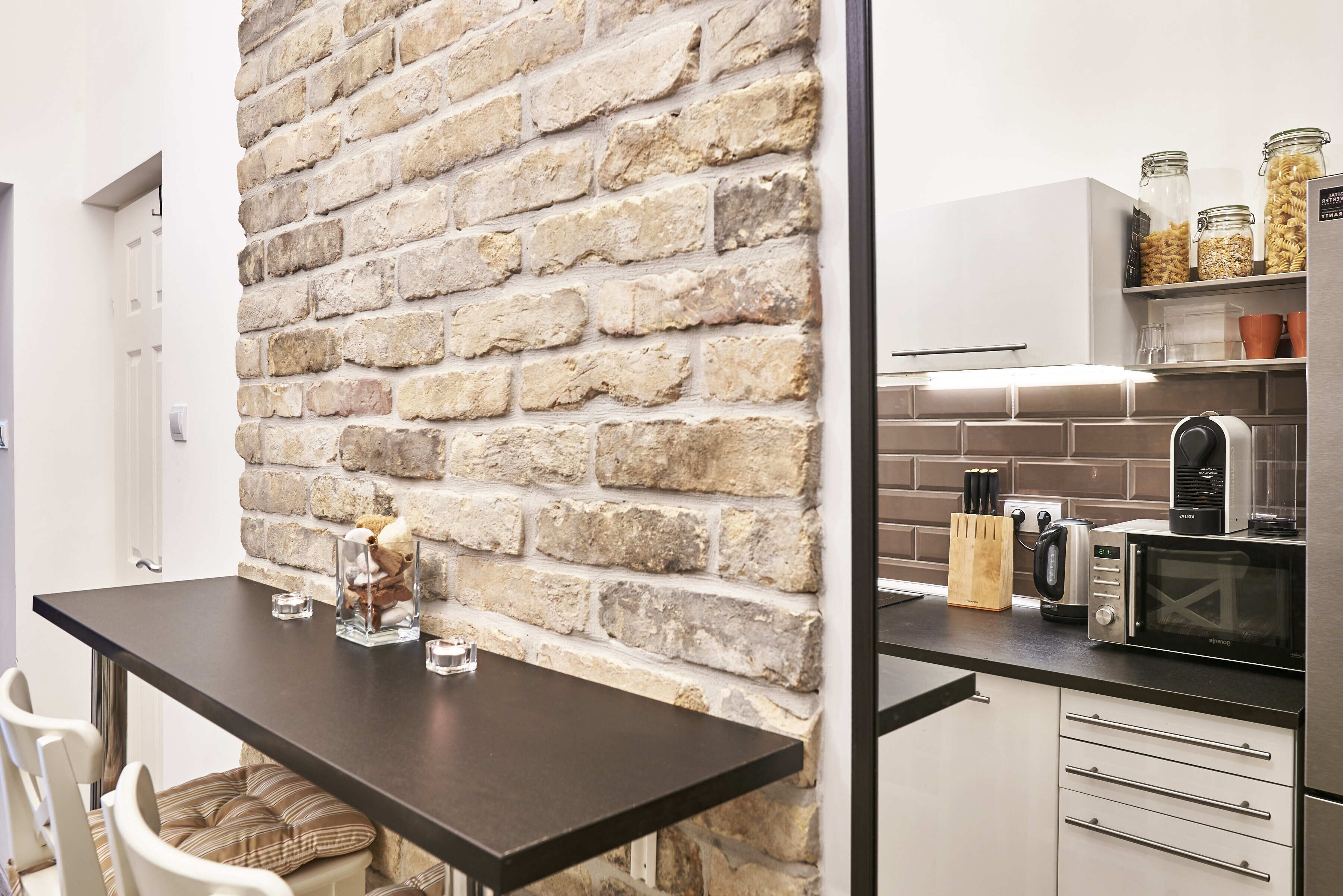 A kitchen with a brick wall, a dark countertop, and various appliances including a microwave and toaster.