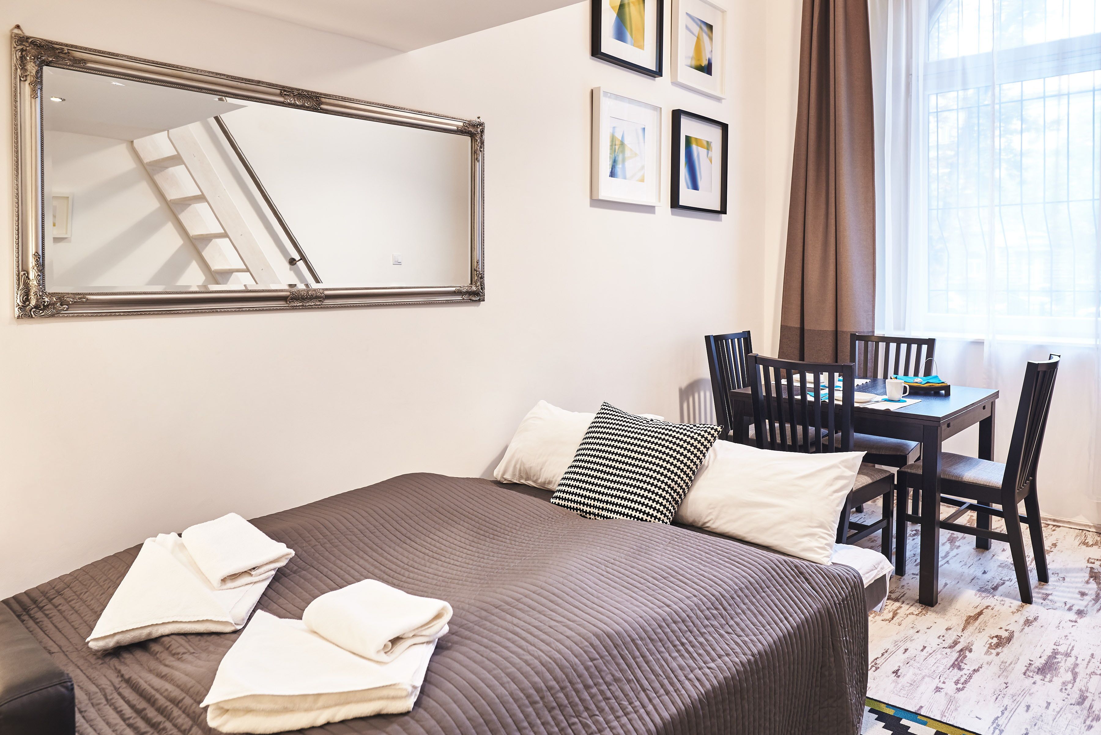 Ein Hotelzimmer mit einem großen Bett, einem Esstisch mit Stühlen, einem Spiegel und gerahmten Kunstwerken an der Wand.