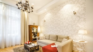 A living room with a sofa, a small table, a lamp, a bookshelf, and a chandelier. - Magas 5 Apartment (Budapest)