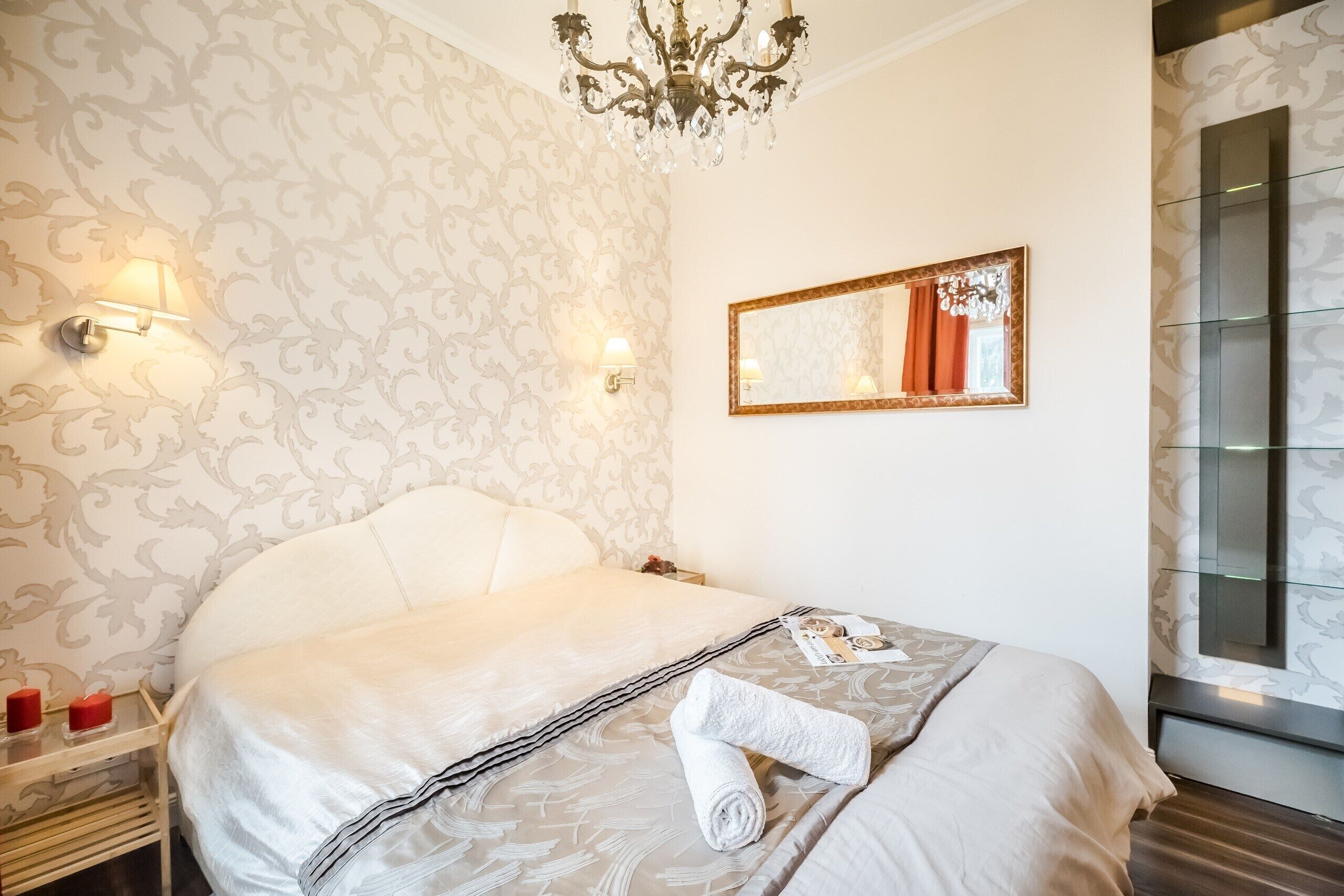 Ein Hotelzimmer mit einem großen Bett, einer Kristallleuchter, einem Spiegel und einem Nachttisch mit einer Lampe.