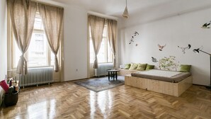 A spacious room with a wooden floor, a bed with green pillows, a small round table, and a radiator. - Molnar 21 Apartment (Budapest)