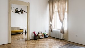 A room with a herringbone floor, a sofa, a chair, a radiator, a window with curtains, and a mirror with a monkey decoration. - Molnar 21 Apartment (Budapest)