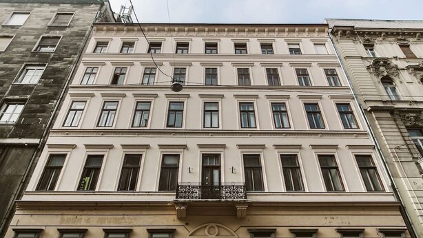 Un edificio de varios pisos con fachada simétrica, grandes ventanales y una entrada central con arco decorativo.