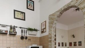 Una cocina con microondas, armarios y salpicadero de azulejos. Se aprecia un arco de piedra que da acceso a un comedor con mesa y sillas.