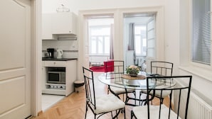 A compact kitchen with white cabinets, a microwave, and a coffee maker. There is a dining area with a glass table and black chairs. - Nagy Diofa 18 Apartment I. (Budapest)