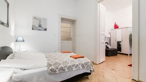 A bedroom with a bed, a nightstand, a lamp, a door leading to a bathroom, and a small table with a red object on it. - Nagy Diofa 18 Apartment I. (Budapest)