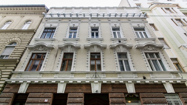 A multi-story building with a symmetrical facade, featuring a central entrance with a decorative archway and a series of windows on each floor. - Nagy Diofa 18 Apartment I. (Budapest)